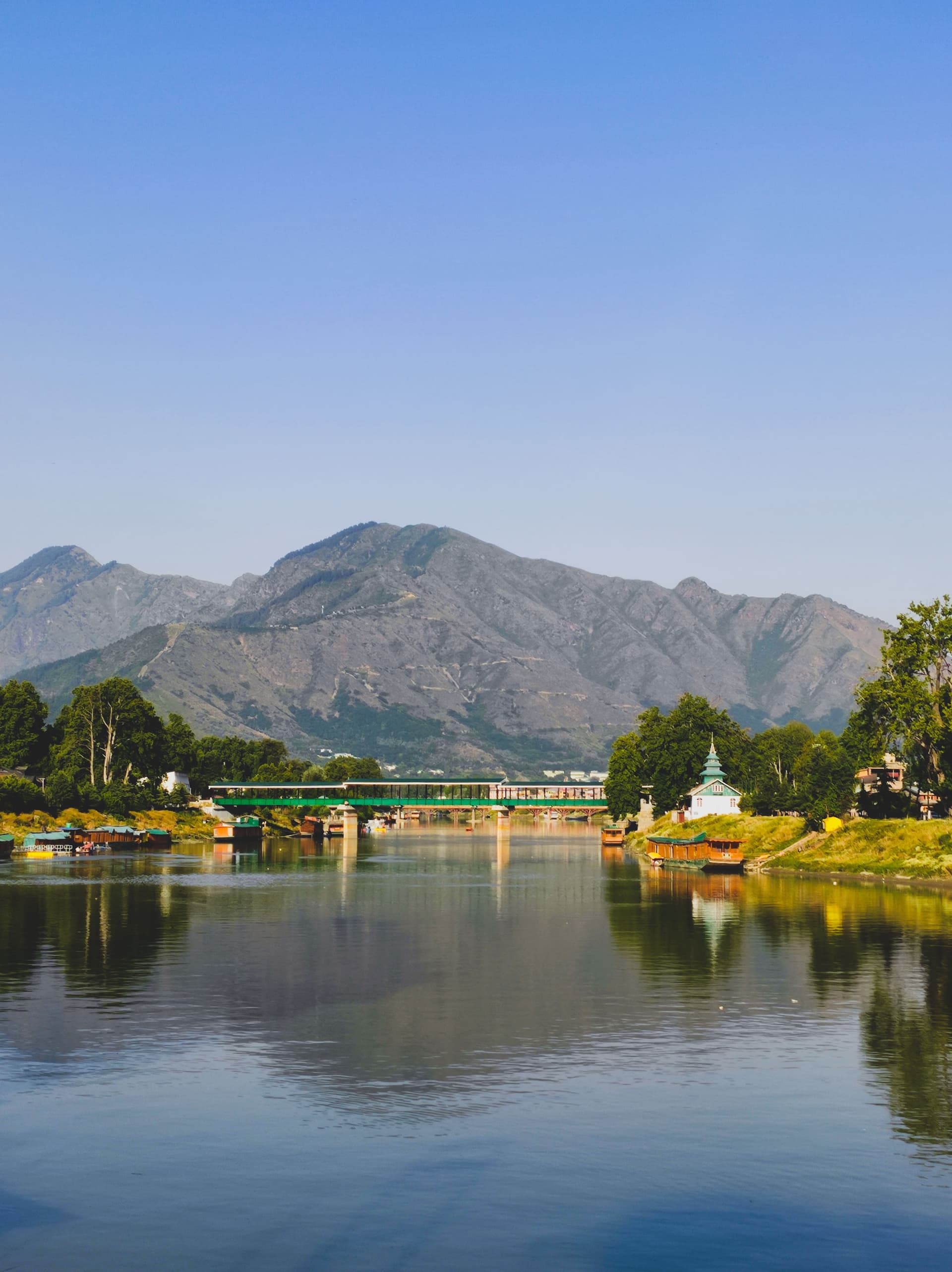 A waterway with boats and a bridge beneath Kashmir’s mountains